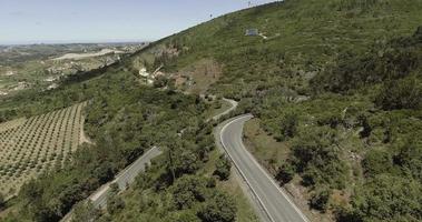 volando sobre la carretera en la exuberante montaña en reguengo do fetal en batalha, portugal con vista lejana del monumento nacional de la fundación panam - drone aéreo video