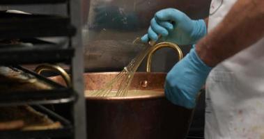 Baker Wearing A Blue Gloves, Stirring Using Egg Whisk On A Deep Copper Pan. - Wide Shot video