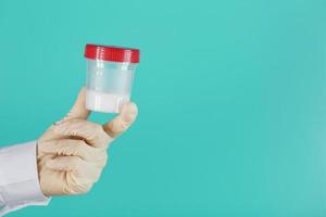 Semen in a jar for analysis in the doctor's hand on a blue background. photo