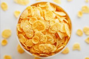 White cup with golden corn flakes, isolated on white background. Hopya crumbled around the cup. View from above photo