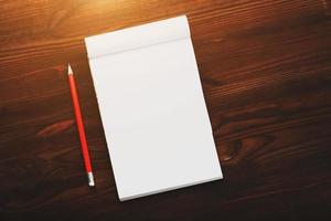 Notebook with a red pencil on a brown background with warm sunlight, for writing. Free empty space for writing on a blank sheet of a notebook. photo