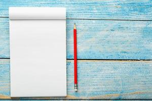 Notepad with red pencil on a blue wooden table background, for education, write goals and deeds photo