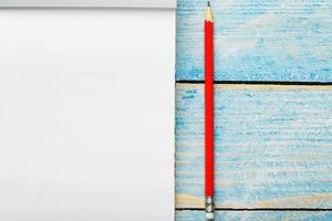 Notepad with red pencil on a blue wooden table background, for education, write goals and deeds photo