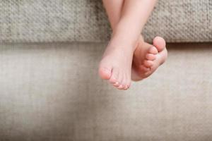 Children's legs close-up hanging from the sofa in the room. Baby toes while baby is sitting on the armchair photo