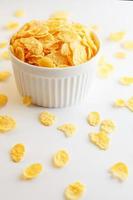 White cup with golden corn flakes, isolated on white background. Hopya crumbled around the cup. View from above photo