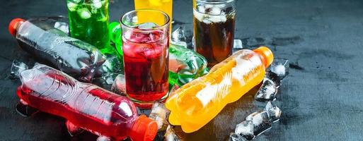 vista superior muchas botellas de refrescos coloridos y sabrosos en la mesa, vasos con bebidas dulces con cubitos de hielo foto