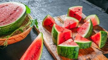 fruta de sandía fresca cortada en trozos en una tabla de cortar de madera, la fruta de sandía se cortó por la mitad, revelando su carne roja brillante. foto