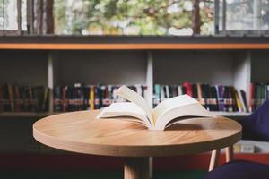 un libro abierto o un libro de texto en la biblioteca con luz de la ventana en la mesa de lectura y el pasillo de las estanterías en el fondo del aula escolar.concepto de aprendizaje educativo foto