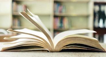 un libro abierto o un libro de texto en la biblioteca con luz de la ventana en la mesa de lectura y el pasillo de las estanterías en el fondo del aula escolar.concepto de aprendizaje educativo foto