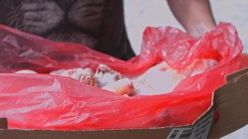 vista de primer plano de las manos en guantes empacando patas de pollo de una caja en bolsas de plástico individuales. proceso de congelación de carne para su uso posterior en el hogar. Video 4k con juego de luces