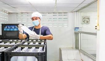 Young man worker or quality inspector in workwear and with a protective mask on his face working in checking bottled drinking water in drink water factory before shipment.drinking water business photo