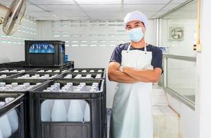 trabajador joven o inspector de calidad en ropa de trabajo y con una máscara protectora en la cara trabajando en el control de agua potable embotellada en la fábrica de agua potable antes del envío.negocio de agua potable foto