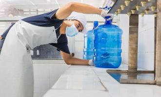 hombre trabajador en ropa de trabajo y con una máscara protectora en la cara trabajando produce agua potable en una fábrica de agua potable limpia. línea de producción de agua potable limpia foto