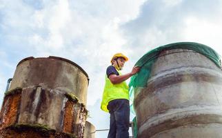 ingeniero que controla la calidad del agua se encuentra en las escaleras de riesgo en lugares altos operando equipos de filtración o purificación de agua industrial viejos tanques de cemento para mantener el agua en la fábrica de agua foto