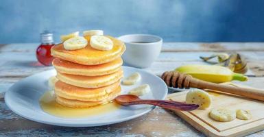 pila de panqueques de plátano con rodajas de plátanos frescos, una pila de panqueques caseros dulces con mantequilla y jarabe para el desayuno en un fondo de madera foto