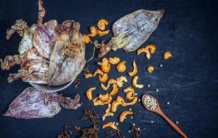 vista superior de mariscos secos con calamares secos y camarones secos sobre una mesa de madera negra. que contiene especias, semillas de pimienta