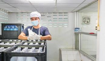 Young man worker or quality inspector in workwear and with a protective mask on his face working in checking bottled drinking water in drink water factory before shipment.drinking water business photo