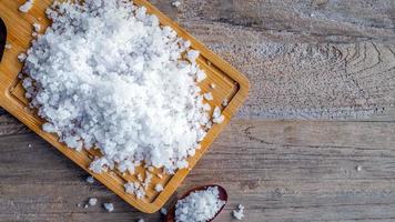 Top view of salt crystals in wooden spoons on old wooden background.Salt flavored condiment salt. photo