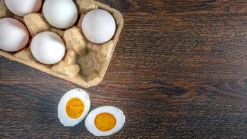 vista superior de los huevos de pato en una caja de huevos y el huevo de pato se corta por la mitad para revelar la yema sobre fondo de madera foto