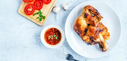 vista superior del menú de pollo a la parrilla con salsa picante sobre fondo blanco de madera foto