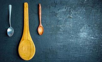 Collection of large wooden spoons with small and stainless steel spoons on black background, top view.