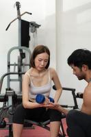 Young couple exercising in a gym When lifting weights, they assist one another. Concept of bodybuilding and healthy living