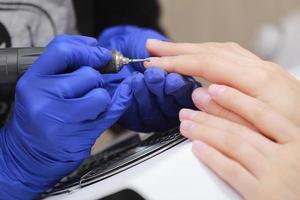 Close Up shot of hardware manicure in a beauty salon. Manicurist in protective gloves is applying electric nail file drill to manicure on female fingers. photo