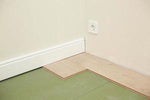Installing wooden laminate or parquet floor in room over green base. assembling panels quickly and easily - affordable flooring. laying laminate flooring at home photo