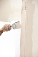 Builder using a trowel to add plaster. Plastering wall with putty-knife, close up image. Fixing wall surface and preparation for painting. construction work during quarantine photo