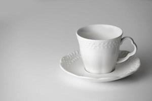 White tea cup and saucer with a pattern for drink on white background. Ceramic coffee cup or mug close up. Mockup classic porcelain utensils. copy space photo