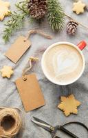etiquetas de regalo en blanco con rama de pino, taza de café y galletas de Navidad sobre fondo textil. el concepto de preparación para las vacaciones de navidad