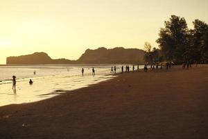 silueta, grupo, de, gente, jugar al fútbol, en la playa, en, el, ocaso, con, seascape, y, montaña, en, plano de fondo foto