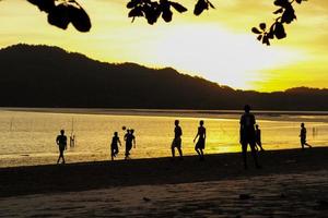 silueta, grupo, de, gente, jugar al fútbol, en la playa, en, el, ocaso, con, seascape, y, montaña, en, plano de fondo foto