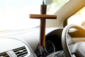 Closeup wooden crucifix hang  in  front steering wheel and console of the car. Concept, talisman,amulet to prevent accidents. Belief, faith,holy  in god to protect when driving. photo