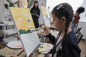 A little girl concentrates on acrylic color picture painting on canvas with student children in an art classroom, creative learning with talents and skills in the elementary school studio education. photo