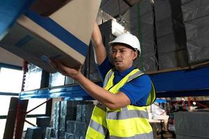 Smart millennial Asian male warehouse worker in his uniform working in warehouse, checking inventory in parcel. shipping warehouse job photo