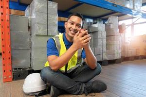 trabajador masculino asiático con uniforme de seguridad hablando por walkie talkie con sus colegas. ingeniero o conductor que trabaja en el centro de distribución de almacenes logísticos. envío y entrega foto