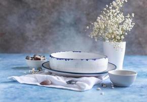 platos blancos de cerámica hechos a mano con rayas azules en el borde, flores secas y conchas marinas vacías sobre fondo de hormigón azul. foto