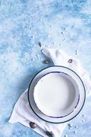 Handmade ceramic white plates with blue stripe on the edge and empty seashells on blue concrete background. Top view. photo