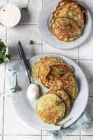 buñuelos de verduras servidos con hierbas frescas y salsa, fondo de mosaico gris. panqueques vegetarianos de brócoli o espinacas. vista superior. foto