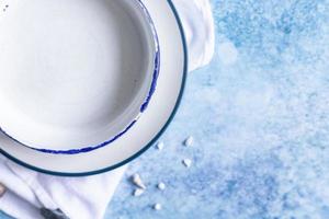 placas blancas de cerámica hechas a mano con rayas azules en el borde y conchas vacías sobre fondo de hormigón azul. vista superior. foto