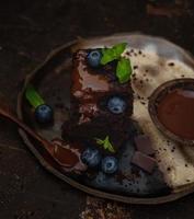 Dark chocolate brownie with blueberry, mint, chocolate sauce and pieces of bitter chocolate. Tasty homemade fudge and chewy dessert with melting chocolate. photo