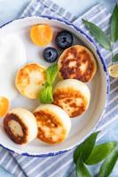 Cheese pancakes, fritters or syrniki with blueberry, physalis and yogurt, blue background. Healthy and tasty breakfast. photo