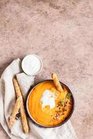 Pumpkin and carrot soup with cream, mint and seeds, brown concrete background. Traditional autumn or winter vegetarian soup with a creamy silky texture. photo