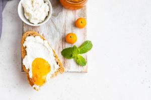 Sliced artisan homemade bread with ricotta or cottage cheese and orange jam on light background. Tasty breakfast. High key photography. photo