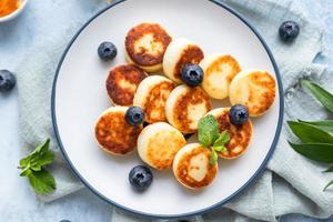 Cheese pancakes, fritters or syrniki with blueberry, physalis and yogurt, blue background. Healthy and tasty breakfast. photo