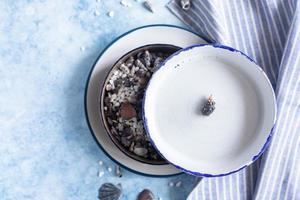 Handmade ceramic white plates with blue stripe on the edge and empty seashells on blue concrete background. Top view. photo