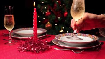 frau, die champagnerflötenglas auf einen geschmückten roten tisch für das weihnachtsabendessen setzt