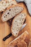 Sliced round rustic bread without kneading on a cutting board next to a knife. Homemade whole grain bread, layout on the table, vertical frame photo