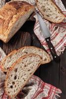 Round rustic bread without kneading cut into pieces on a cutting board on an old dark rustic table. Homemade whole grain bread, layout on the table, vertical frame photo